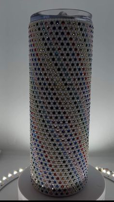 a glass vase with multicolored dots on it sitting on a white pedestal next to some lights