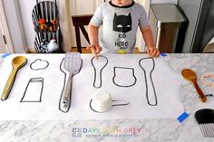 a young boy standing in front of a table with utensils on top of it