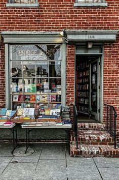 an old brick building with books on display in the window and behind it is a table full of books