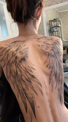 the back of a woman's upper half with an angel wing tattoo on it