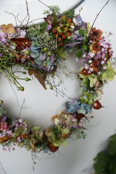 a heart shaped wreath made out of flowers and leaves on top of a white vase