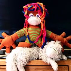 a stuffed animal with long hair sitting on top of a dresser next to another stuffed animal