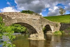 an old stone bridge over a river under a cloudy sky