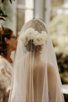 a woman wearing a veil with flowers in her hair is standing next to another woman