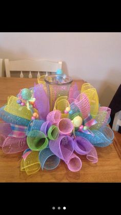 a colorful mesh wreath sitting on top of a wooden table next to a glass vase