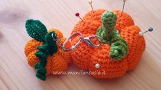 two crocheted pumpkins sitting next to each other on a wooden surface with pins in them