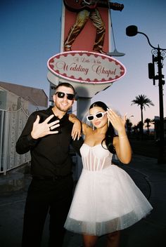 a man and woman posing in front of a wedding chapel sign