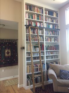 a living room filled with lots of books on top of a white book shelf next to a couch