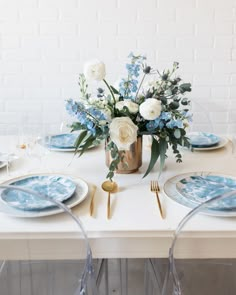 a table set with blue and white plates, silverware and flowers in a vase