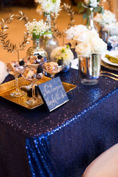 a table topped with desserts and flowers on top of a blue cloth covered table