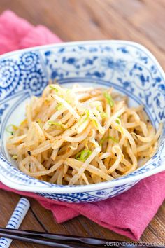 a blue and white bowl filled with food next to chopsticks on a wooden table