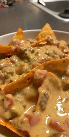 nachos with cheese, meat and sauce in a white bowl