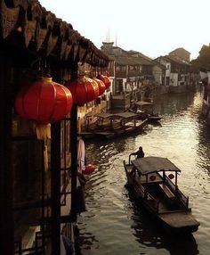 a boat traveling down a river next to houses and lanterns hanging from the side of buildings