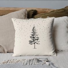 a white pillow with a black and white pine tree on it, sitting on a bed