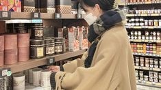 a woman wearing a face mask is shopping in a grocery store while looking at goods on shelves