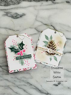 two tags with holly designs on them sitting on a marble surface, one has a christmas ornament hanging from it