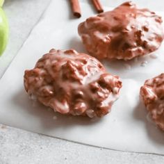 three chocolate covered donuts sitting on top of a piece of paper next to an apple