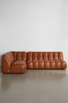 a brown leather couch sitting on top of a cement floor next to a white wall