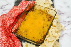 a glass dish filled with cheese and tortilla chips on top of a table