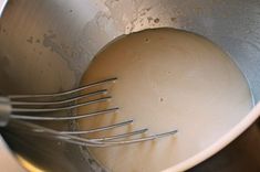 a metal mixing bowl filled with white liquid and whisked utensils in it