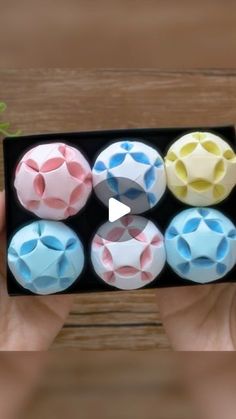 a person holding a small box with six different colored balls in it's center