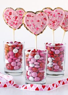 heart shaped lollipops in glass cups with candy on sticks and sprinkles