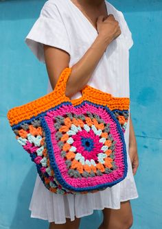 a woman is holding a crocheted bag in front of a blue wall with an orange handle