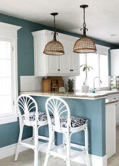 two white bar stools sitting in front of a kitchen island with three lights hanging over it