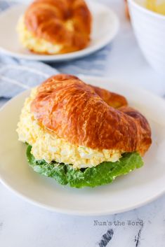 a croissant sandwich with lettuce and eggs on it sitting on a plate