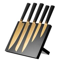 four knives are on a black cutting board with gold handles and blades in the center