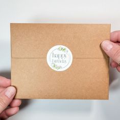 two hands holding a brown envelope with a happy birthday sticker on the front and bottom