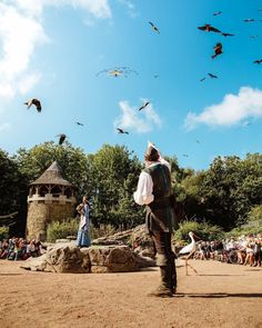 a man standing in front of a group of birds flying over a park filled with people