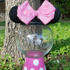 a minnie mouse head with a pink bow and polka dots on it sitting in front of a tree