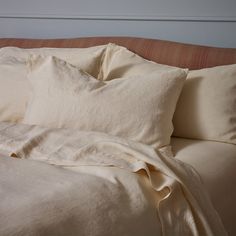 an unmade bed with white linens and pillows on it's headboard