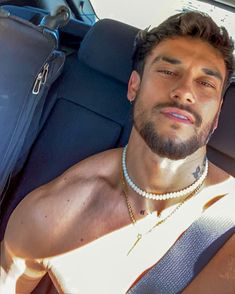 a man wearing a pearl necklace sitting in the back seat of a car