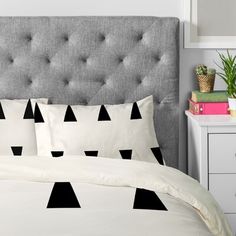 a bed with black triangles on it and white sheets in front of a gray headboard