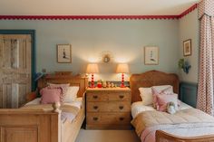 two twin beds in a bedroom with pink and blue decor on the walls, along with wooden dressers