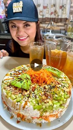 a woman sitting at a table with a large cake on it and drinks in front of her