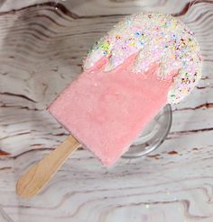 a pink ice cream with sprinkles on top in a glass bowl next to a wooden spoon