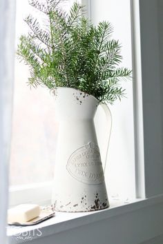 a white vase sitting on top of a window sill next to a book and plant