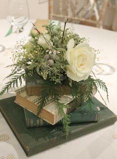 a bouquet of flowers sitting on top of two books at a table with wine glasses