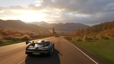 a black sports car driving down a road with mountains in the backgrouund