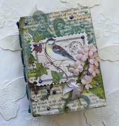 an altered book with flowers and a bird on it's cover is sitting on a white tablecloth