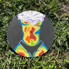 a frisbee that is laying in the grass with a painting on it's side