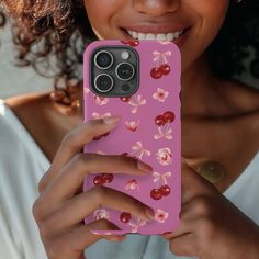 a woman holding up a pink phone case with cherries on it and smiling at the camera