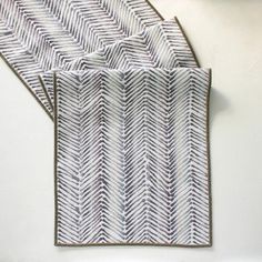 two placemats made out of white and grey herringbone fabric on top of each other