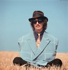 a man sitting in the middle of a field wearing a suit and tie with sunglasses on