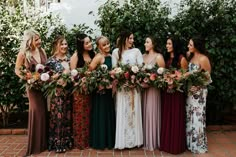 a group of women standing next to each other holding bouquets in front of trees