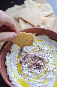 a hand dipping a cracker into a bowl of hummus