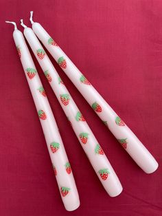 four white candles with strawberries on them sitting on a pink cloth covered tablecloth